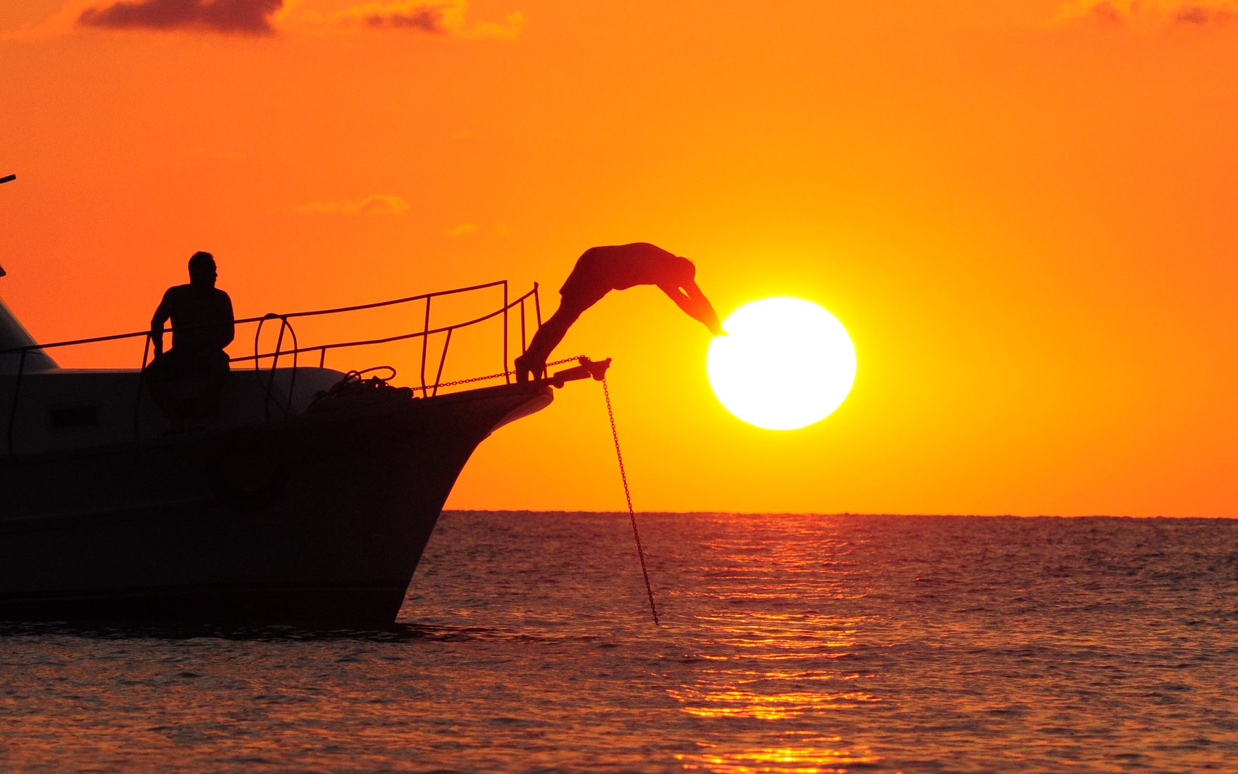 Fishing boat at sunset, its flag dipping toward the sun above a glitter path on the water