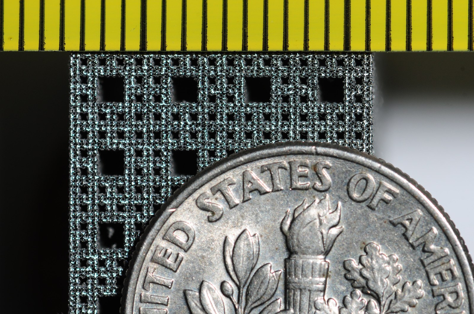 Printed Ti-6Al-4V lattice face beside a US dime and a millimeter scale