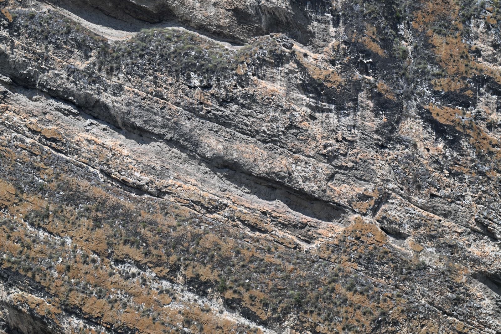 Diagonal strata of gray rock crossed by ochre lichen bands and dark seams, Safranbolu