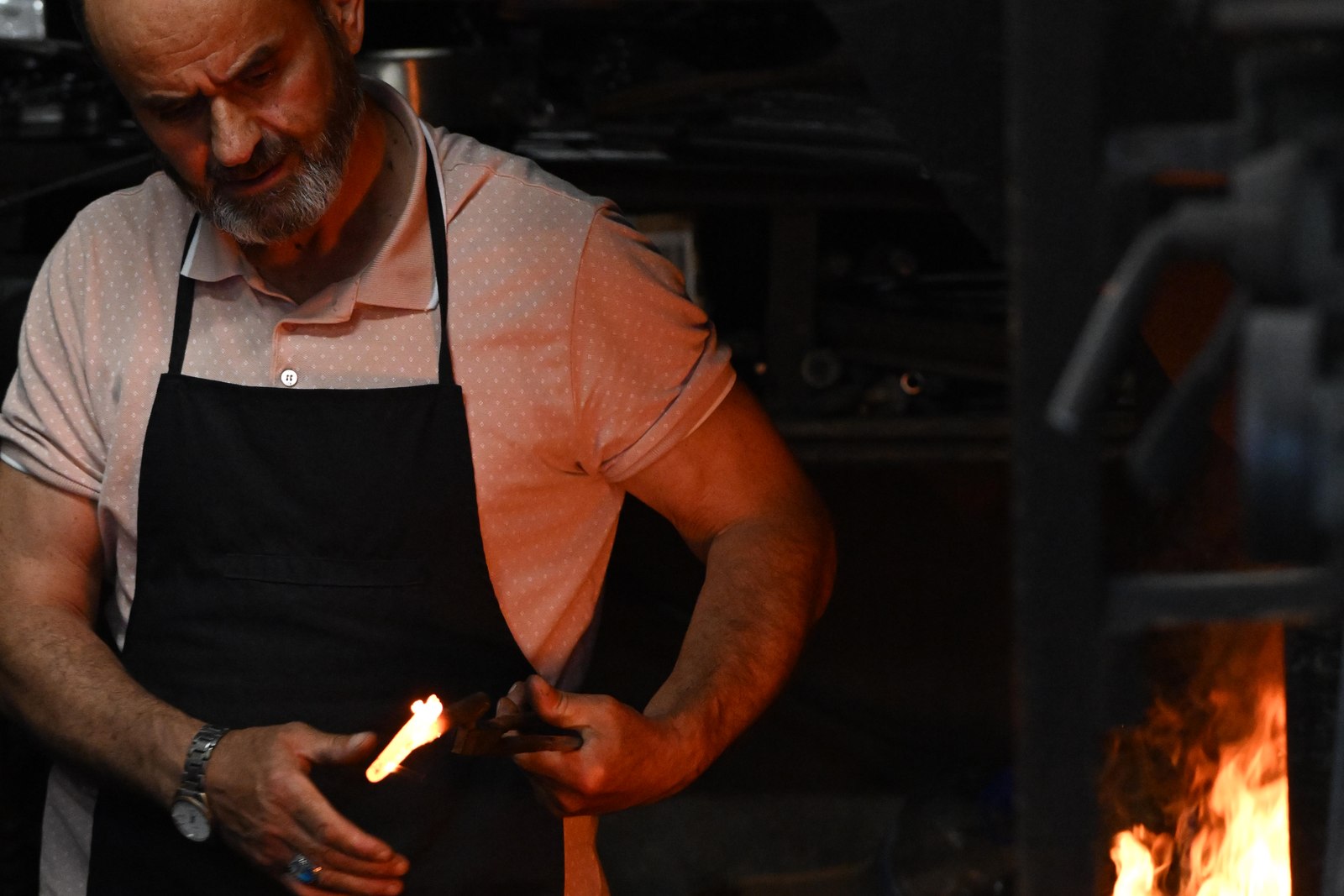 Master blacksmith at his forge, holding a flaming iron with the fire glowing beside him